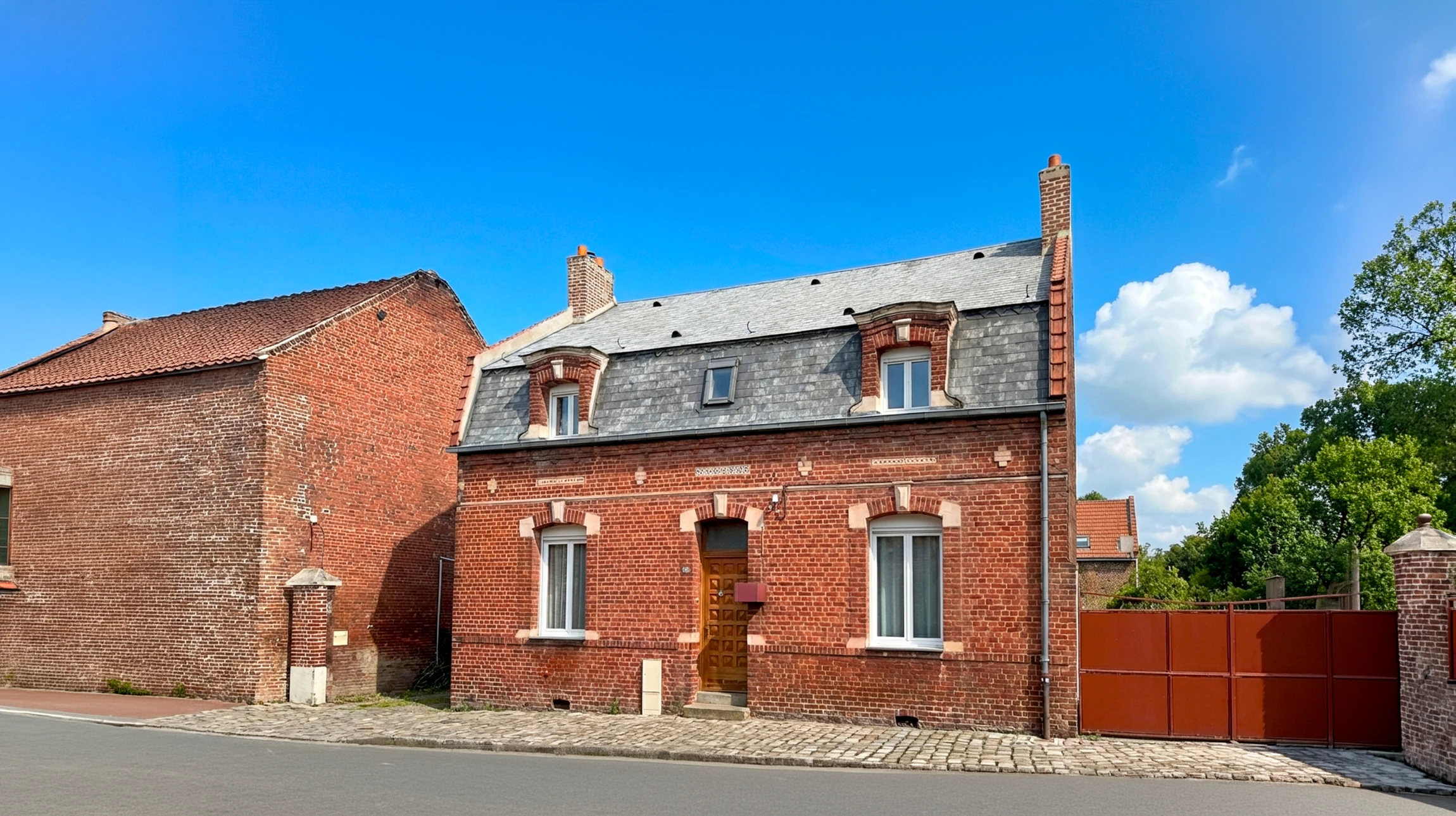 Toiture métallique moderne avec cheminée en acier gris sous ciel nuageux au coucher du soleil, environnement résidentiel boisé